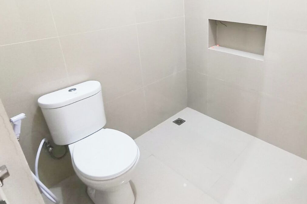 Un baño pequeño y limpio con inodoro blanco, un estante pequeño encima y piso de baldosas.