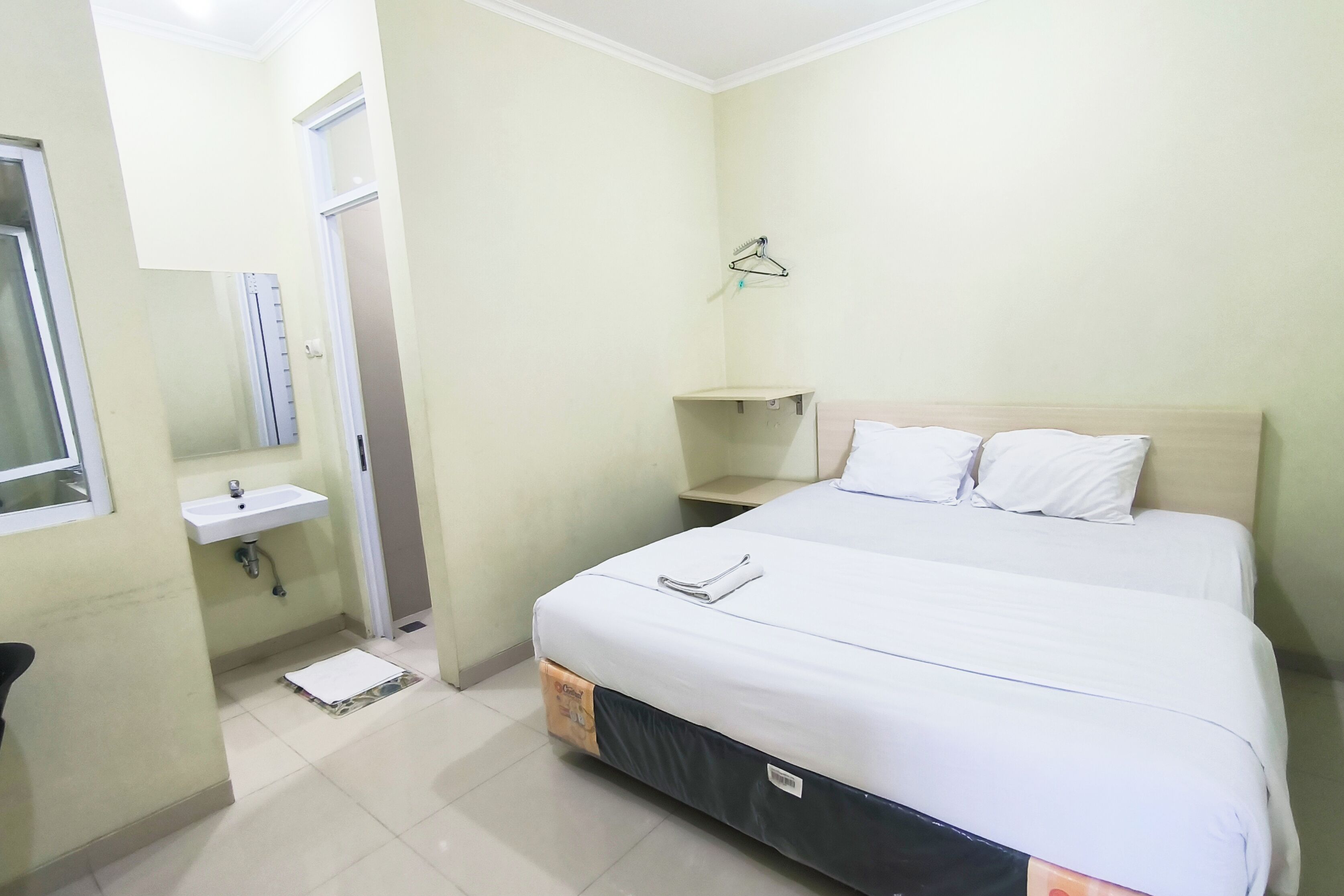 A hotel room with a bed, a bedside table, a hanging light, a window, a sink, and a mirror.