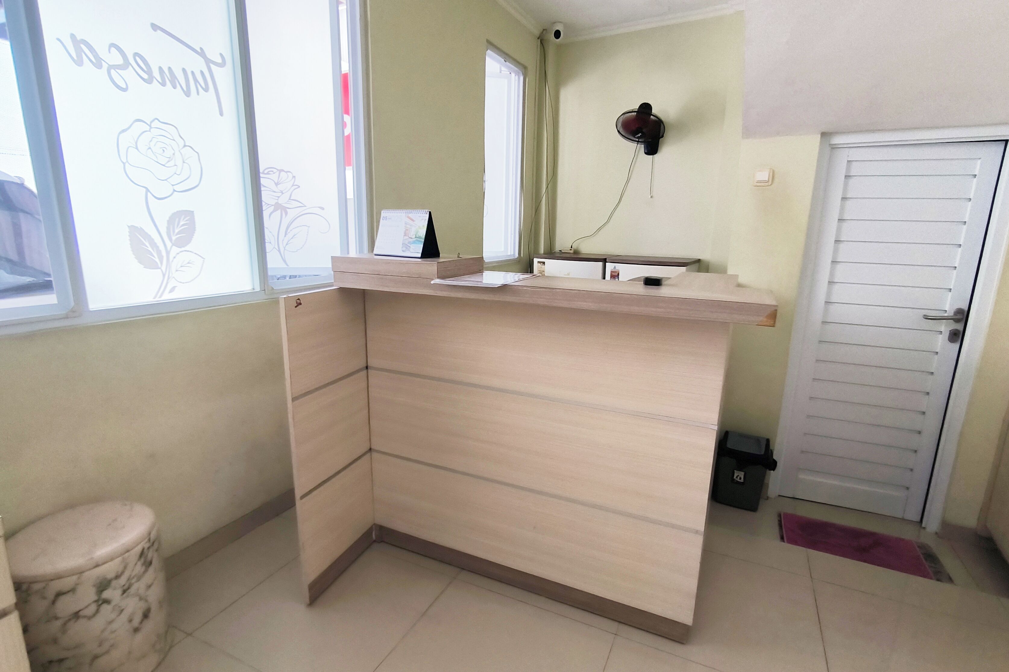 A room with a wooden counter, a small trash bin, a door, and a window with a rose drawing.