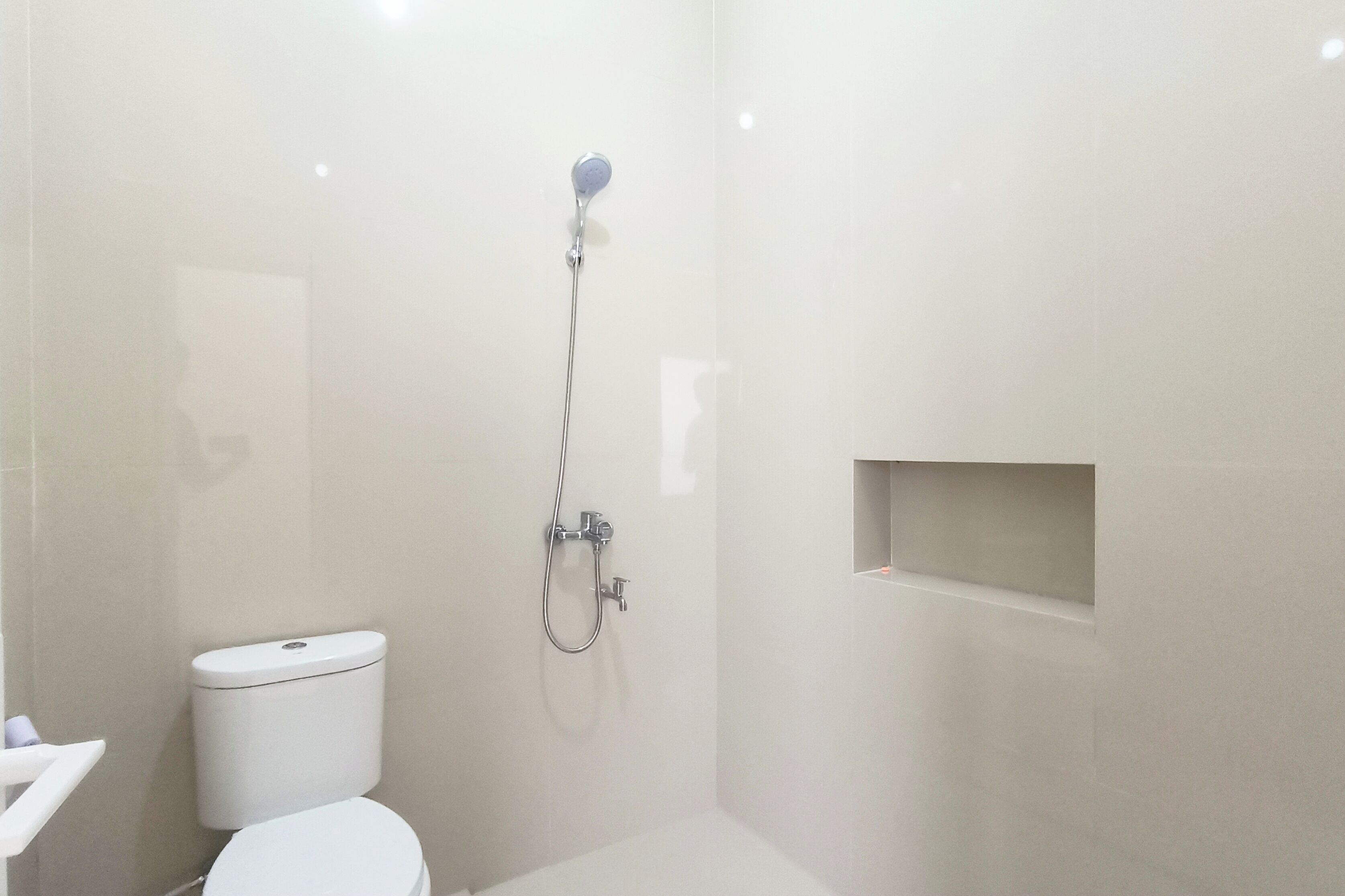 Un baño pequeño y moderno con inodoro, ducha y estante empotrado.