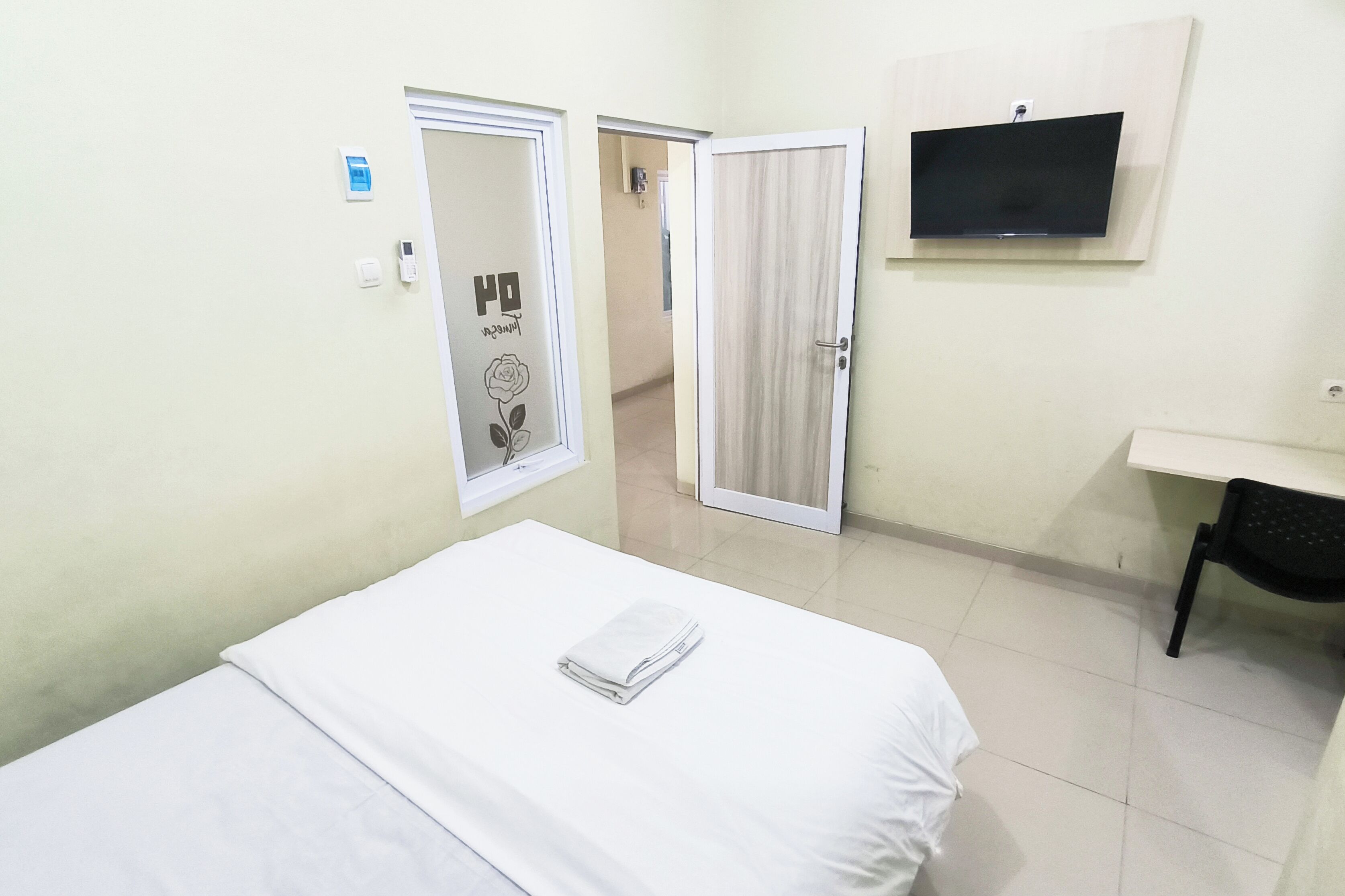 A hotel room with a bed, a desk, a TV, and two doors.