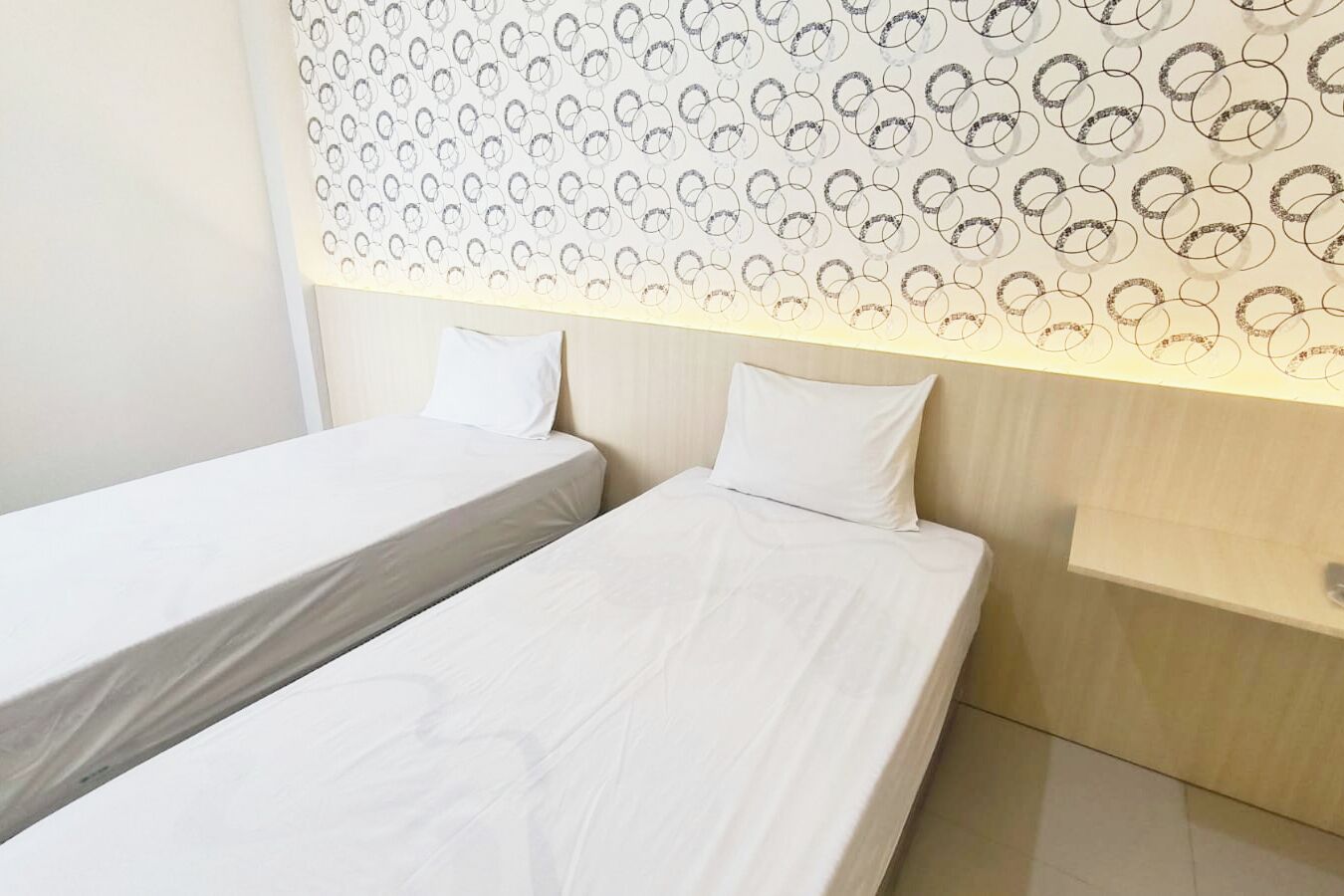 A hotel room with two single beds, a wooden headboard with a circular pattern, and a white wall.