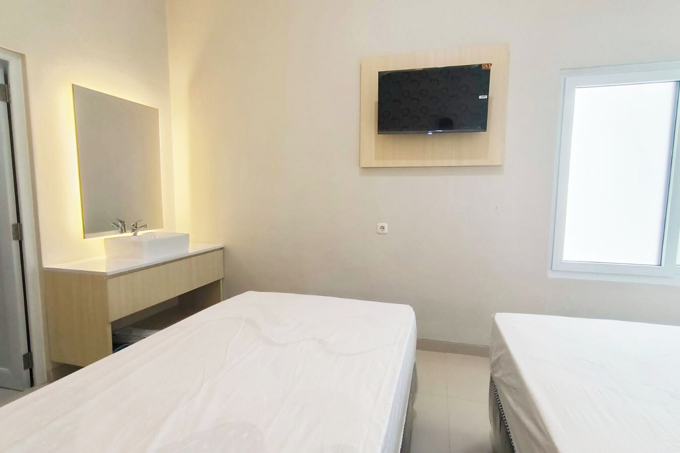 A hotel room with a large bed, a bedside table, a mirror, a TV mounted on the wall, a window, and a bathroom with a sink and mirror.