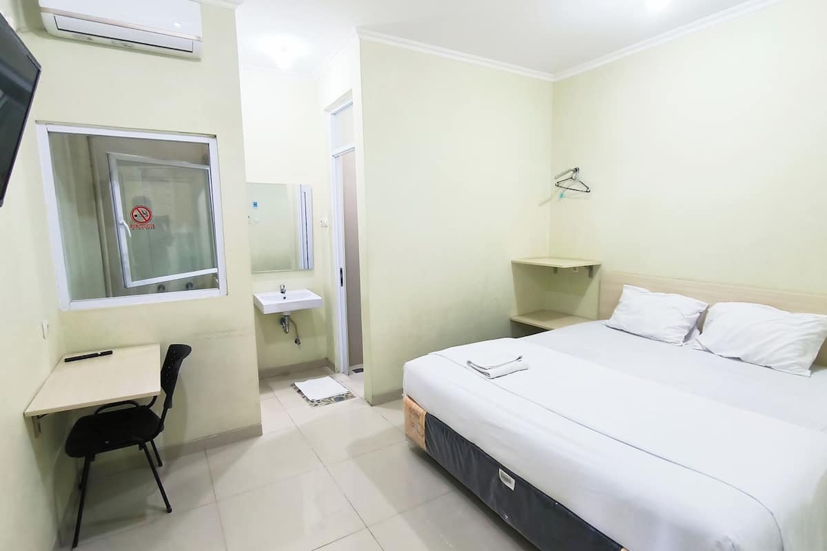 A hotel room with a bed, a desk, a chair, a sink, and a mirror.