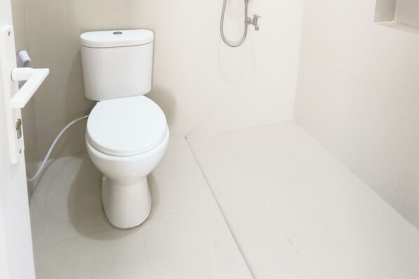 Une petite salle de bain propre, avec des toilettes blanches, une douche et un lavabo blanc.