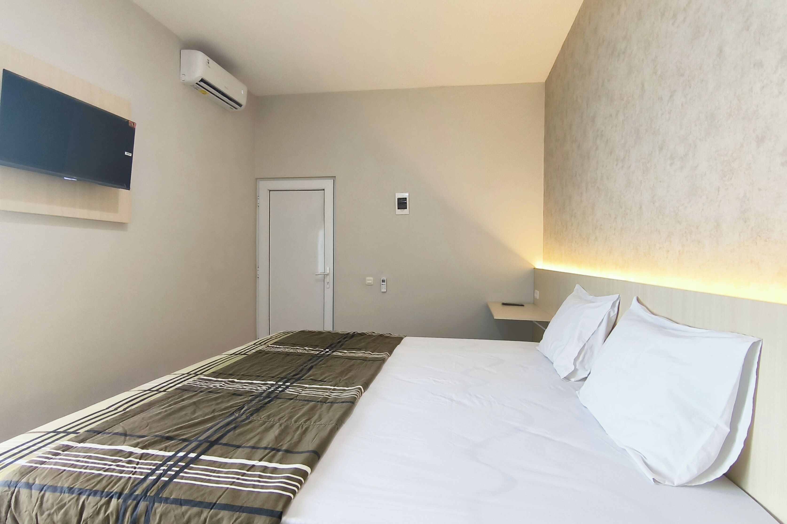 Une chambre d’hôtel équipée d’un lit, d’un téléviseur à écran plat fixé au mur et d’un appareil de climatisation.