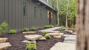 A modern building with a dark exterior, a stone pathway leading to the entrance, and a forested backdrop. - Modern Luxury Retreat · Game Loft · Near Bay (Egg Harbor)