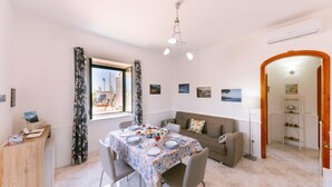 A dining area with a table set for four, a sofa, and a window with curtains. - Infinity Experience Lovely house with sea view terrace (Scala)