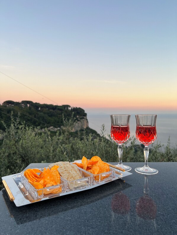 Et bord med snacks og to glas rød drik foran et naturskønt klippelandskab.