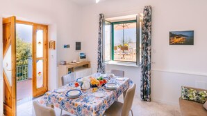 A dining area with a table set for four, a wooden desk, a window with curtains, and a view of the outdoors. - Infinity Experience Lovely house with sea view terrace (Scala)