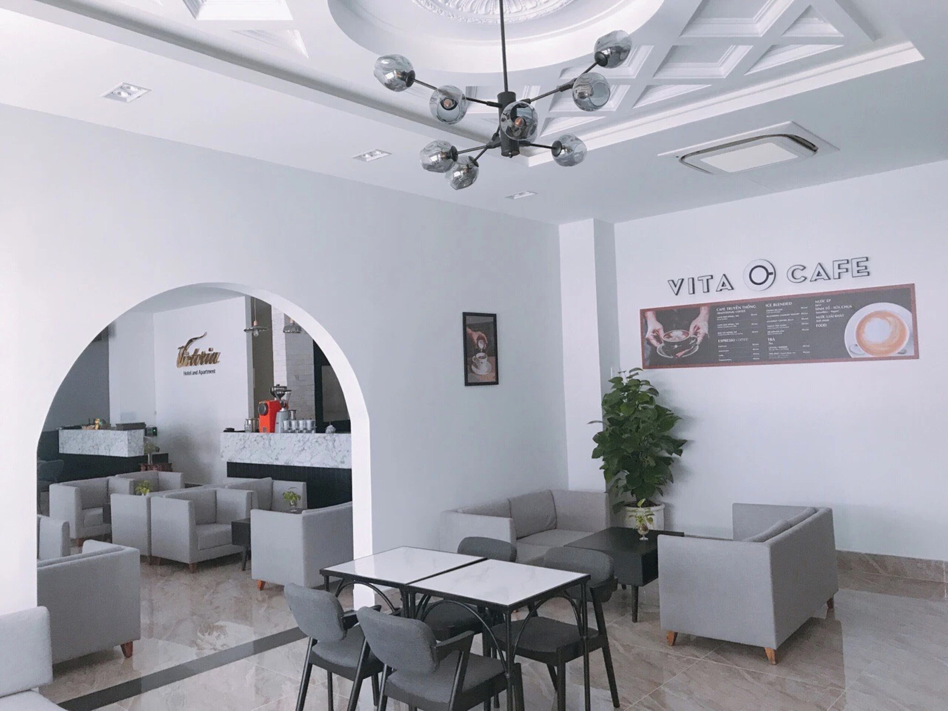 A modern cafe with a marble countertop, seating area with sofas and tables, and a menu board on the wall.