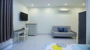 Una habitación pequeña y moderna con escritorio, silla, sofá gris y televisor de pantalla plana montado en la pared.