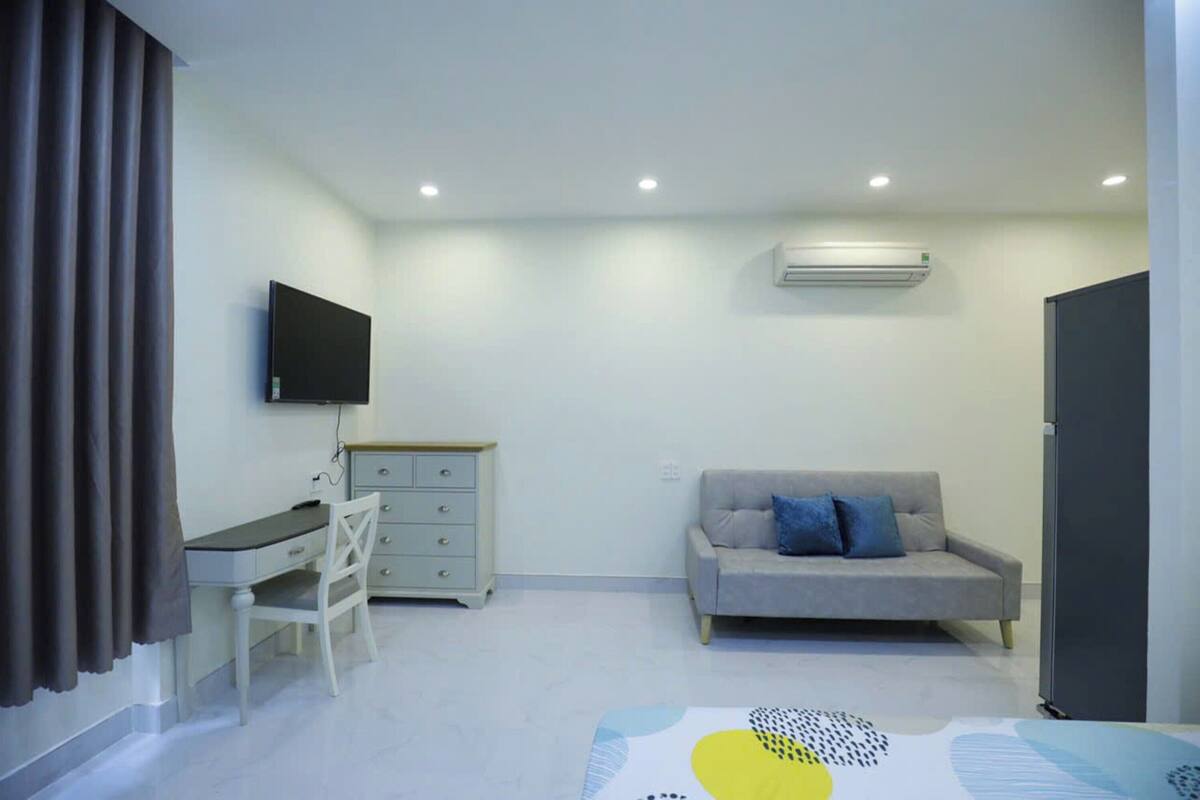 Ein kleiner, moderner Raum mit Schreibtisch, Stuhl, grauem Sofa und einem an der Wand montierten Flachbildfernseher.