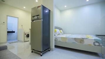 Une chambre à coucher comprenant un lit, un réfrigérateur, un lave-linge et une porte donnant sur une salle de bain.