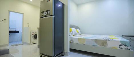 Un dormitorio con cama, refrigerador, lavadora y puerta que da a un baño.