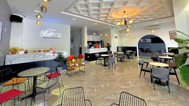 Vestíbulo de hotel con una recepción, áreas de estar y una cocina al fondo.