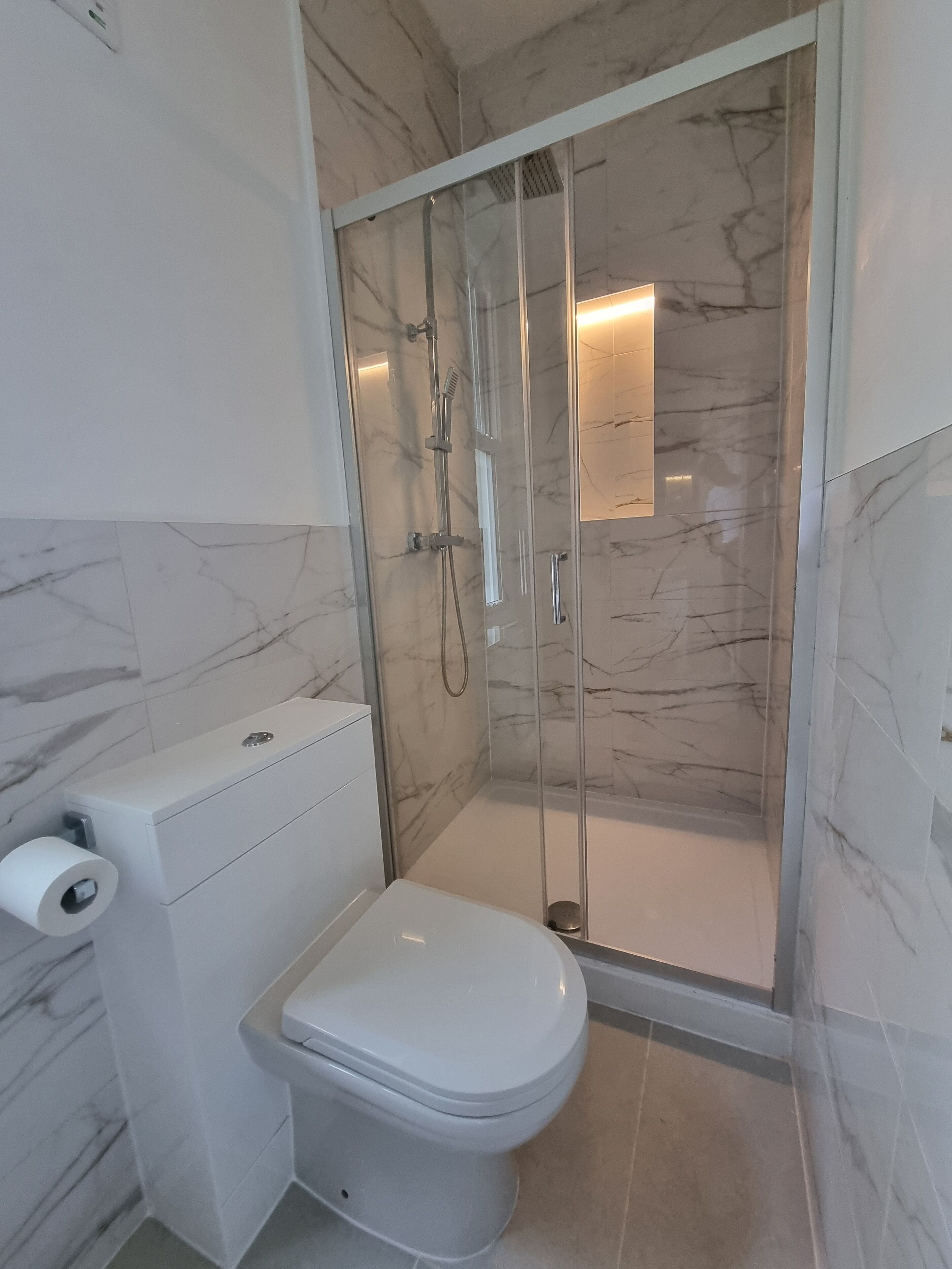 A modern bathroom with a glass-enclosed shower, a toilet, and a marble-tiled wall.