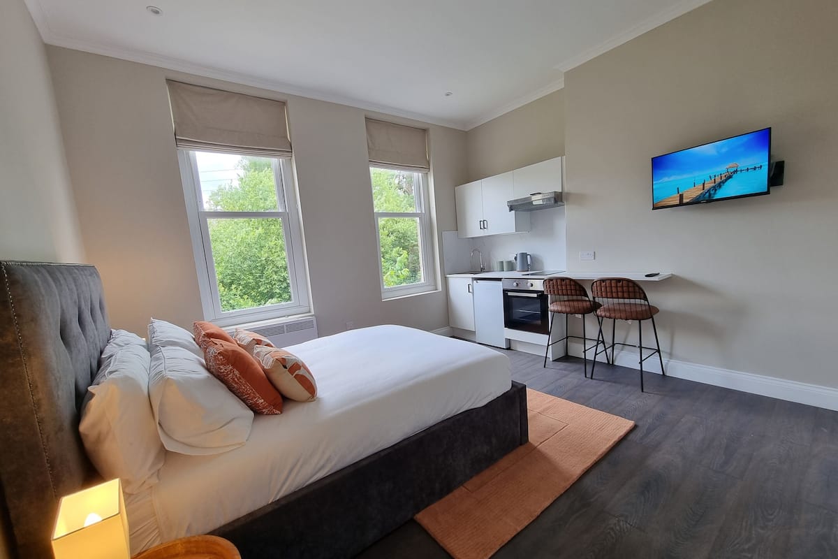 Um quarto moderno com uma cama grande, uma pequena cozinha e uma televisão na parede.