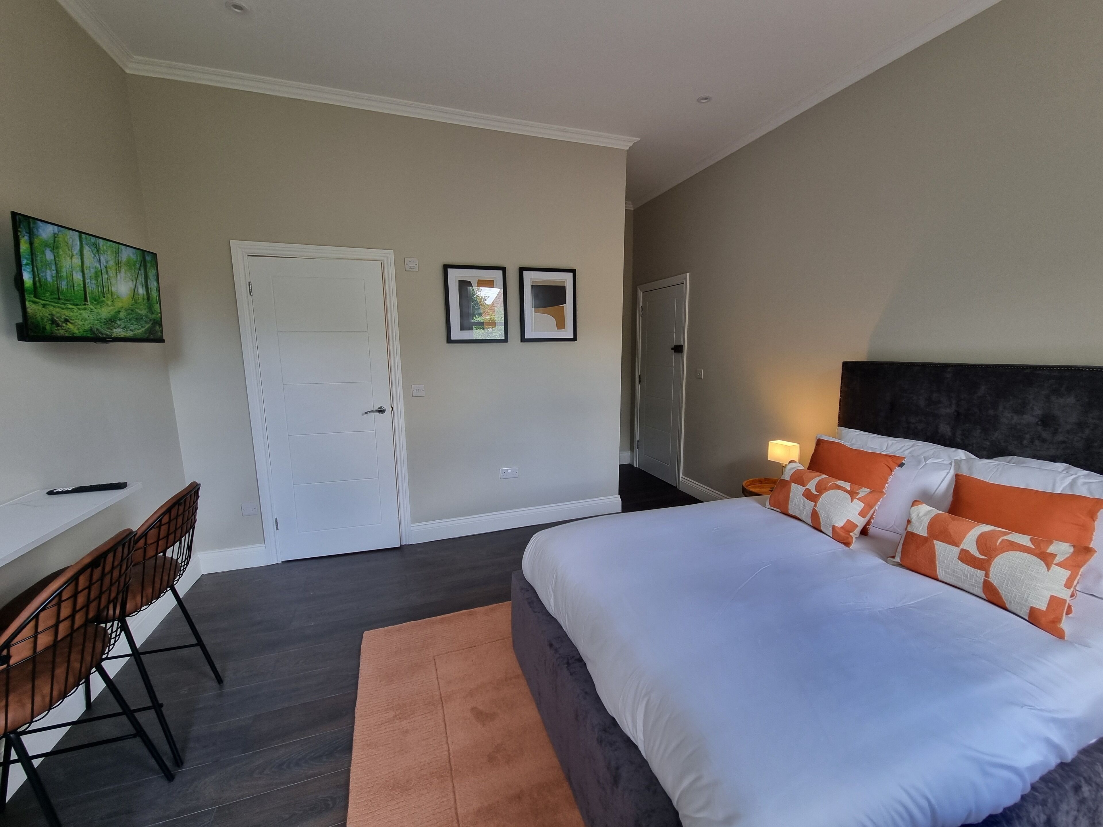 A bedroom with a bed, a desk, and chairs. There are two doors, one of which is open.
