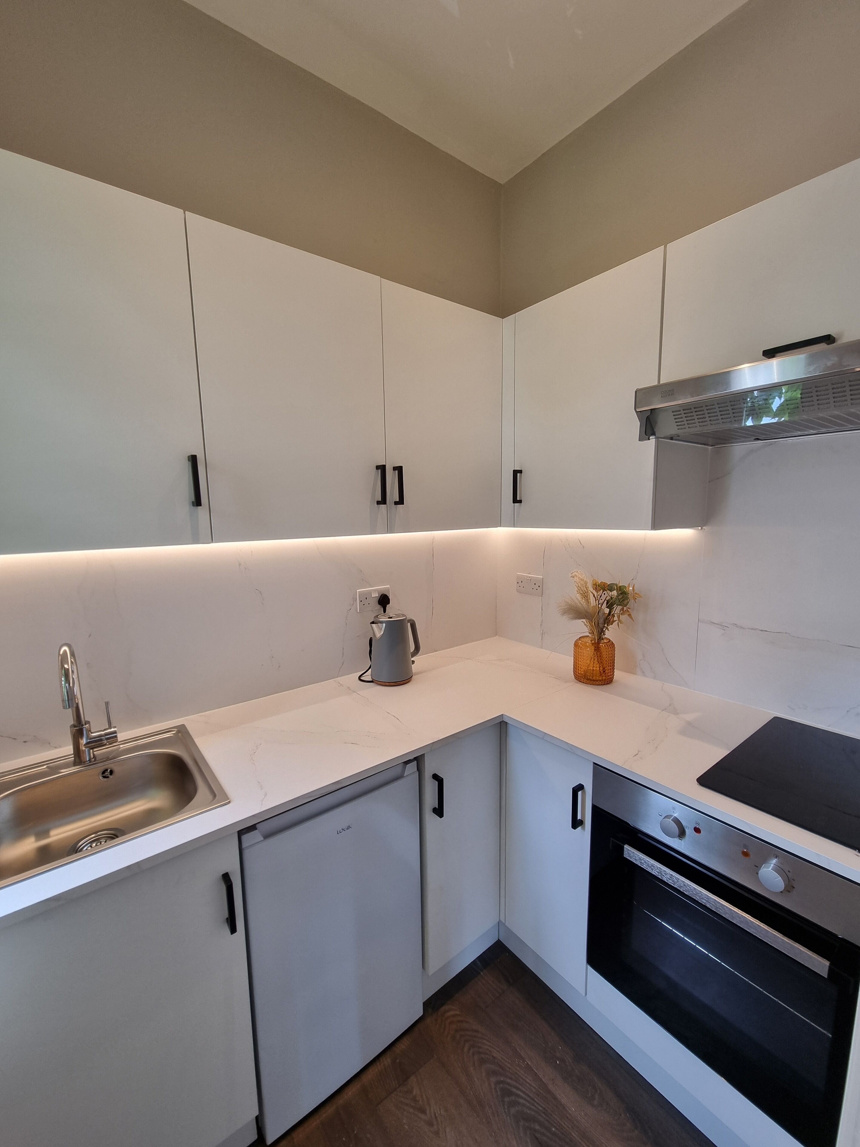 Una cocina moderna con armarios blancos, un lavamanos de acero inoxidable, un hervidor y un horno.
