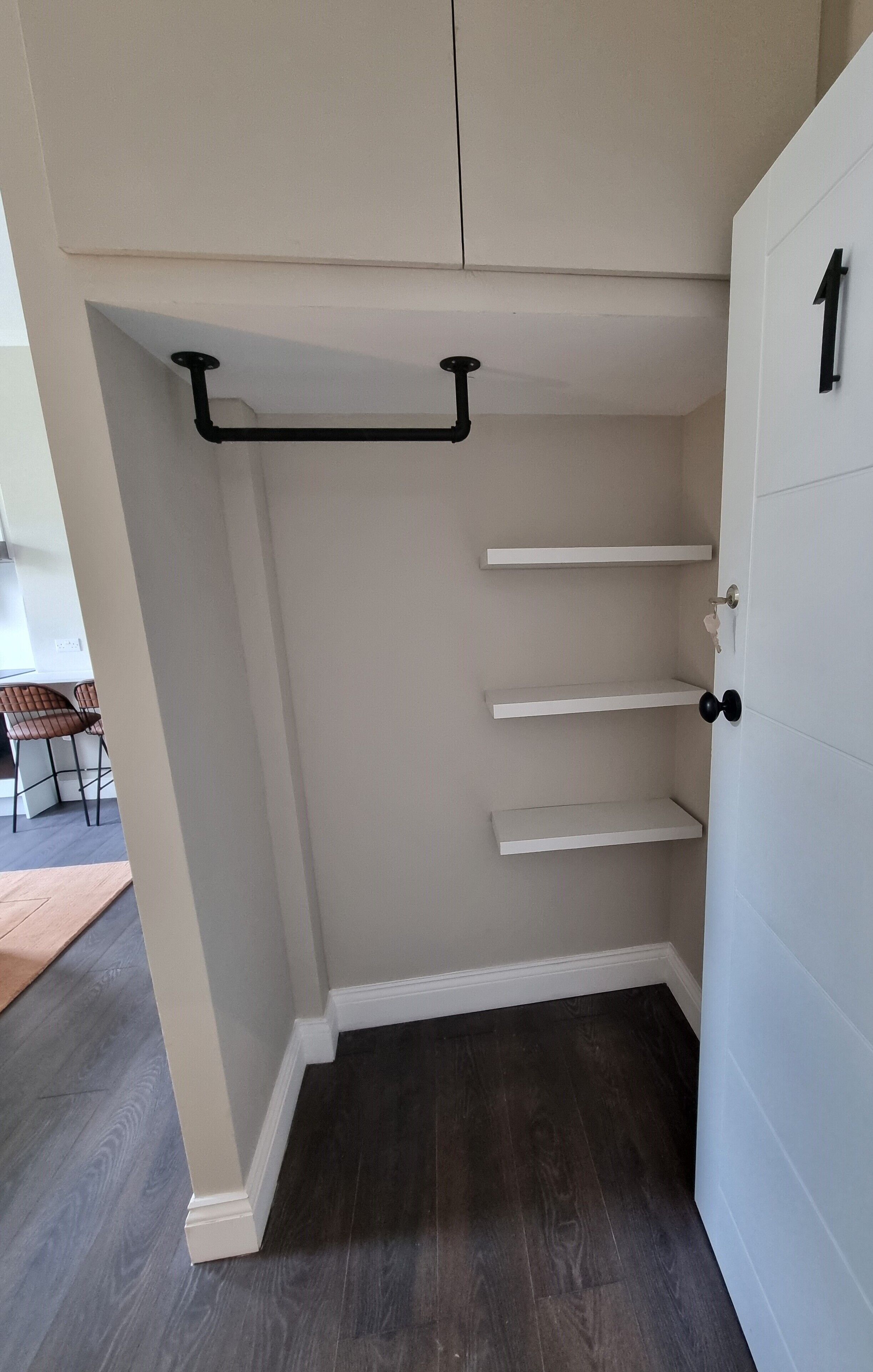 A room with a dark wooden floor, white walls, and a door marked with the number 1.