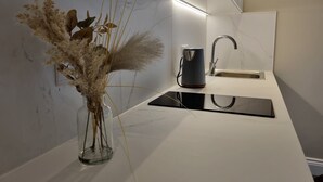 A modern kitchen with a white countertop, a sink, a kettle, and a vase with dried plants. - The Ivy Apartments (Bournemouth)