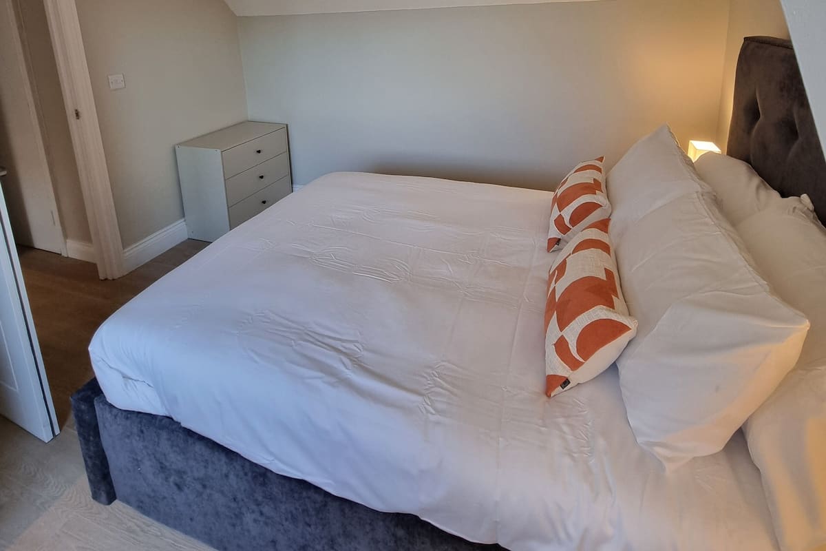 Quarto com cama, almofadas, penteadeira e mesa de cabeceira.