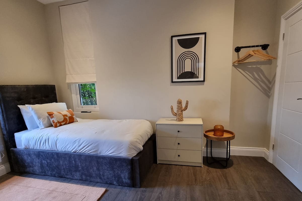 Quarto com cama, mesa de cabeceira e uma pequena mesinha com uma decoração de cacto.