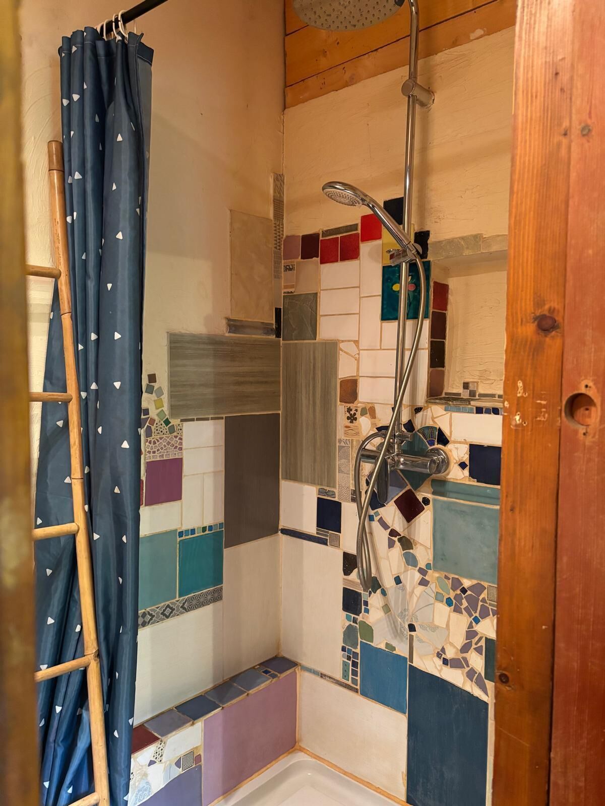A shower with a tiled wall, a showerhead, and a wooden door.
