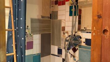 A shower with a tiled wall, a showerhead, and a wooden door.