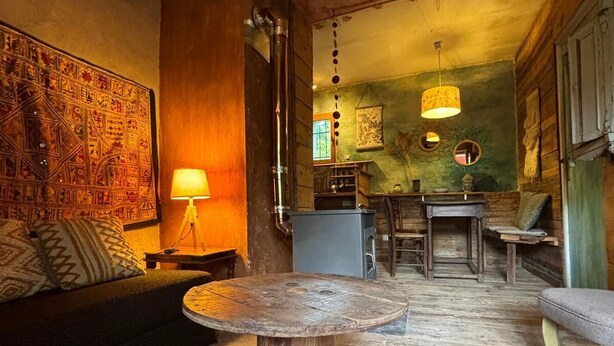 Een rustiek interieur met een ronde houten tafel, een bank en een eethoek met stoelen.