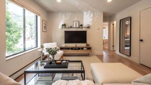A modern living room with a large flat-screen TV, a glass coffee table, and a cozy seating area.