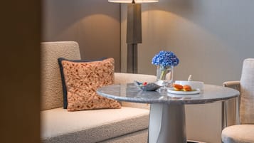 A modern hotel room with a round glass table, a sofa, a lamp, and a trash bin.