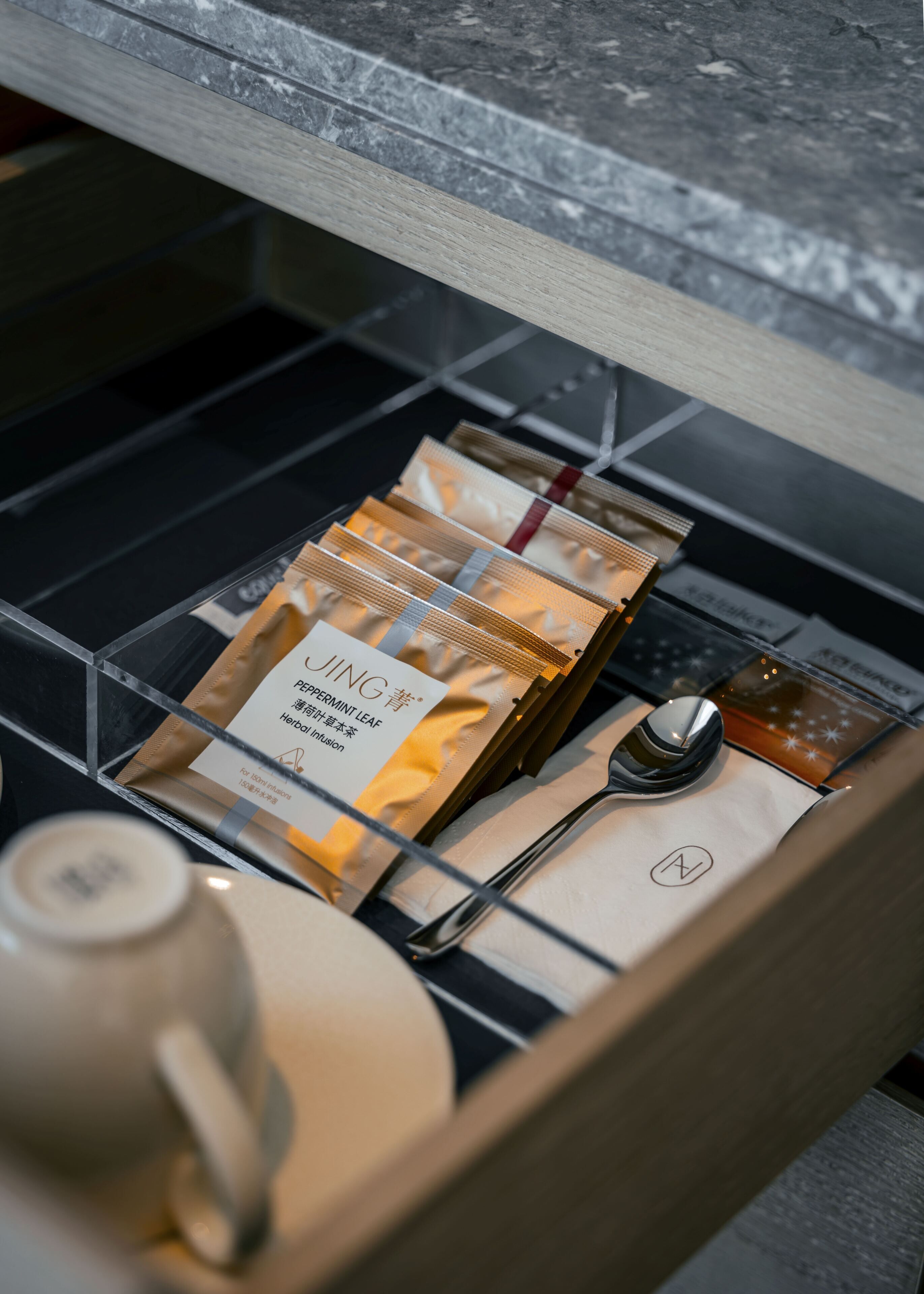 A drawer with neatly arranged items including a tea set, a spoon, and a packet labeled "JING".