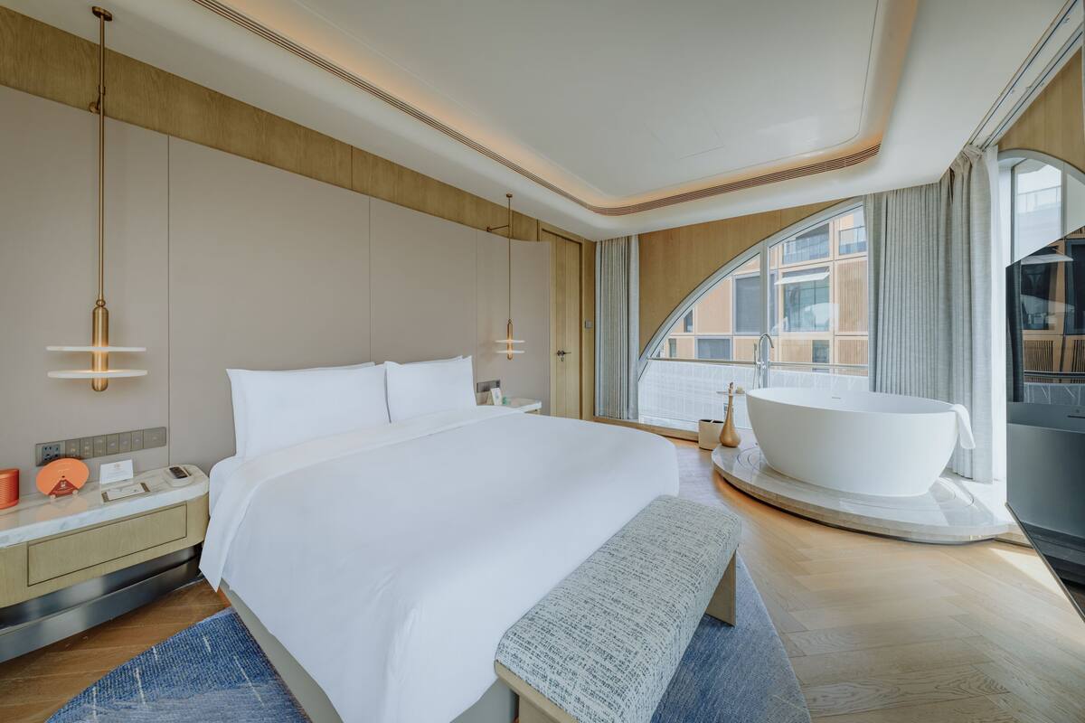 A modern hotel room with a large bed, a bathtub, and a view of the city.