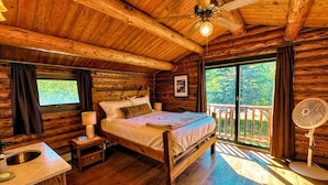 Een slaapkamer in een houten chalet met een bed, nachtkastje, lamp en een raam met gordijnen.