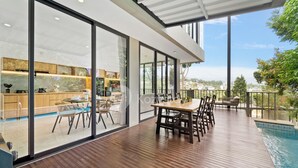 A modern kitchen with large windows, a dining area with a poolside view, and a wooden deck.