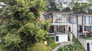 A modern two-story building with balconies, surrounded by lush greenery.