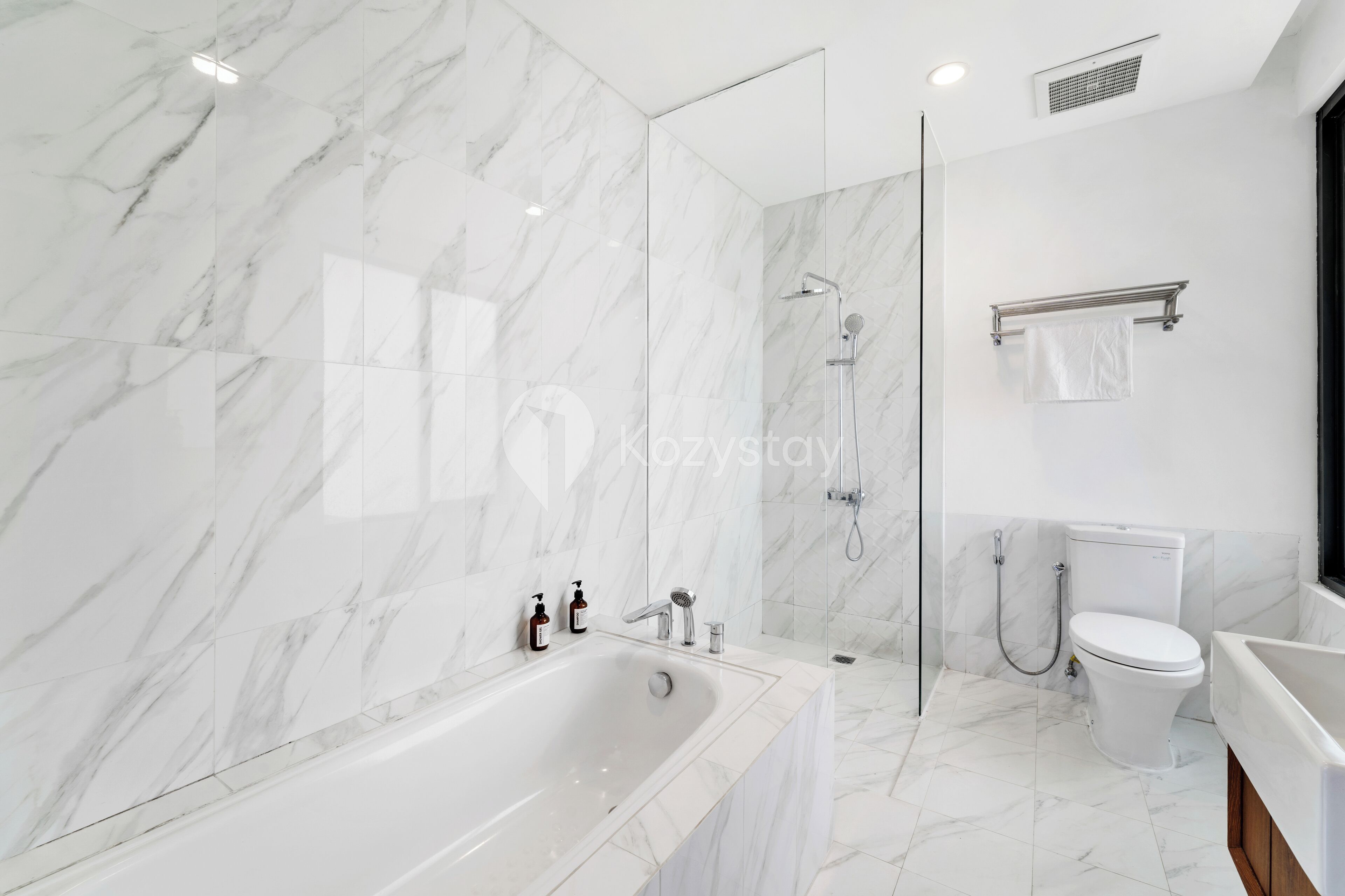 A modern bathroom with a marble wall, a freestanding bathtub, a glass-enclosed shower, and a toilet.