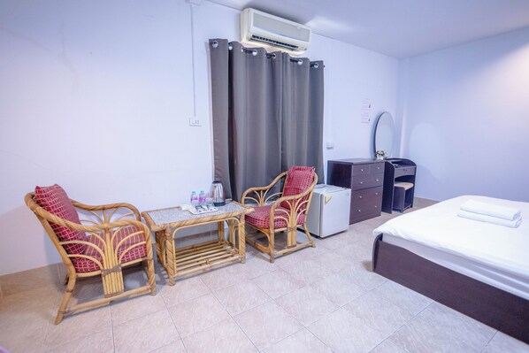 A hotel room with a bed, two wicker chairs, a small table, a desk, a mirror, and an air conditioning unit. - Mitr Inn Hua Hin Beach (Hua Hin)