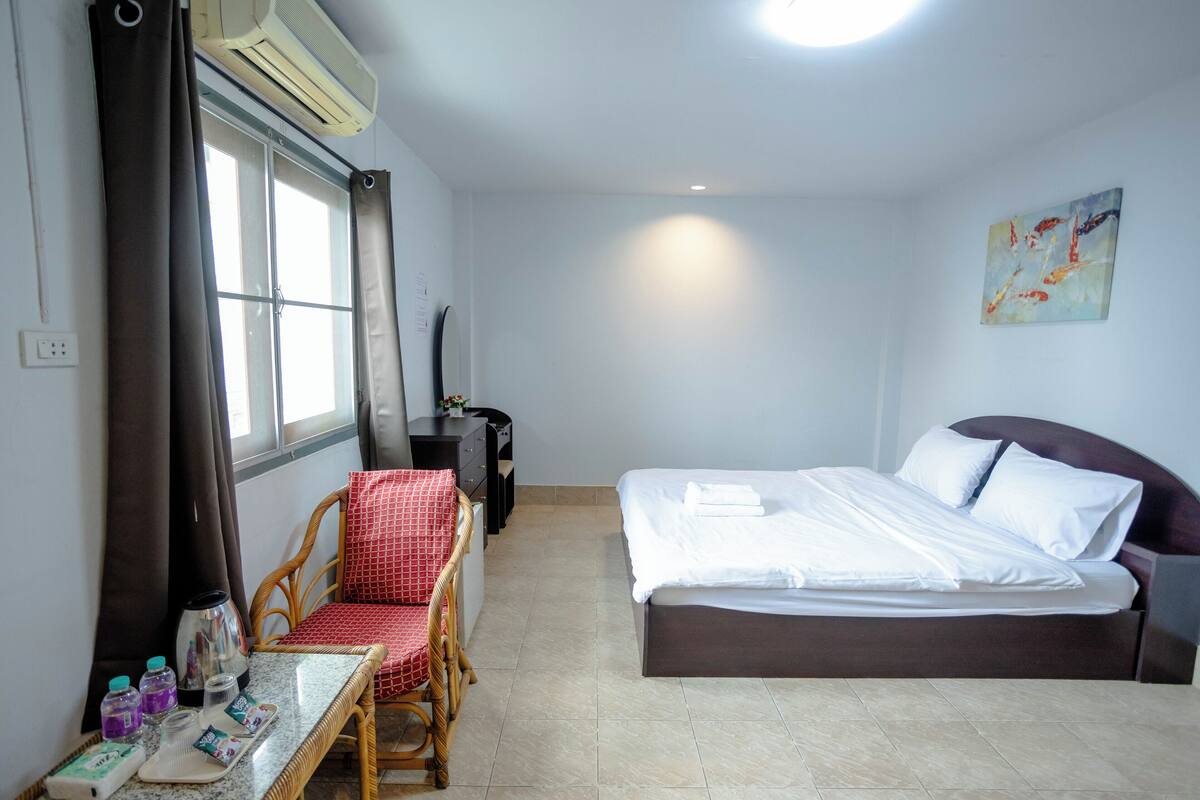 A hotel room with a bed, a chair, a table with toiletries, and a window with curtains.
