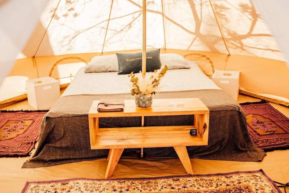 A cozy room with a bed, a bedside table with a vase, and a window with a view of trees.