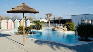 A swimming pool with a thatched umbrella, colorful beach huts, and a white building with a white fence in the background. - The Glamping Spot - Penmarch  (Penmarch)