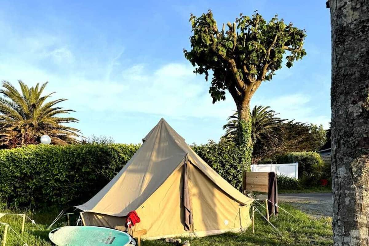 A tent set up on grass with a surfboard and a red object nearby.