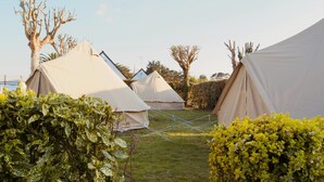A row of beige tents in a grassy area with some greenery and trees in the background. - The Glamping Spot - Penmarch  (Penmarch)