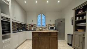 A modern kitchen with white cabinets, a wooden island, a large window, and a microwave. - Window on castle (Monflanquin)