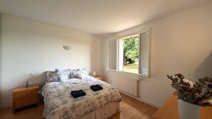 A bedroom with a bed, a nightstand, a window with a view of greenery, and a potted plant. - Window on castle (Monflanquin)