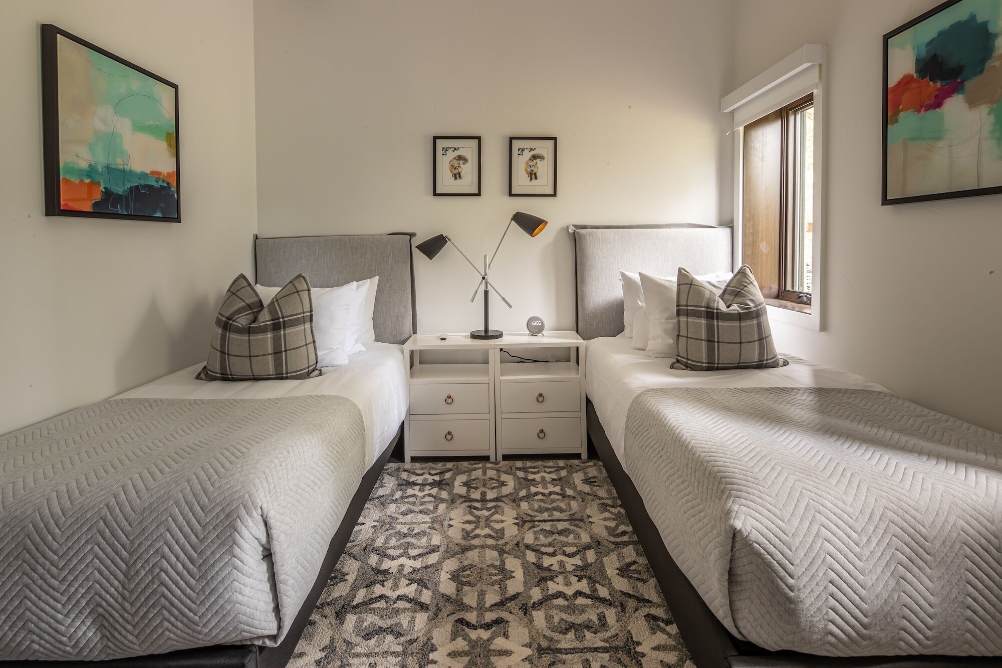 A bedroom with two beds, a nightstand, a lamp, and a rug.
