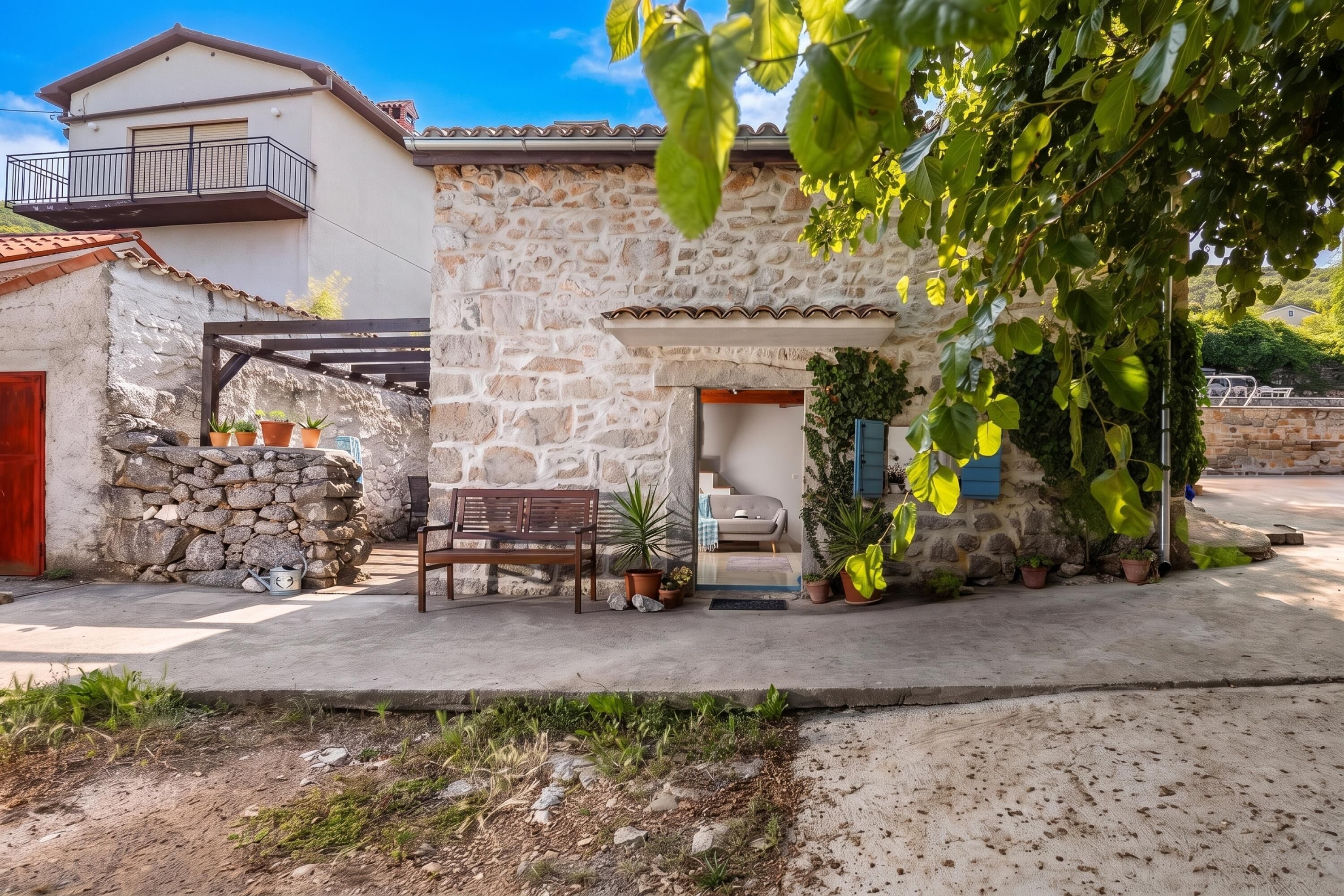 A stone building with a balcony, a wooden bench, and potted plants.