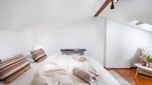 Una camera da letto con soffitto spiovente, un letto con cuscini, un comodino con una lampada e una piccola pianta.